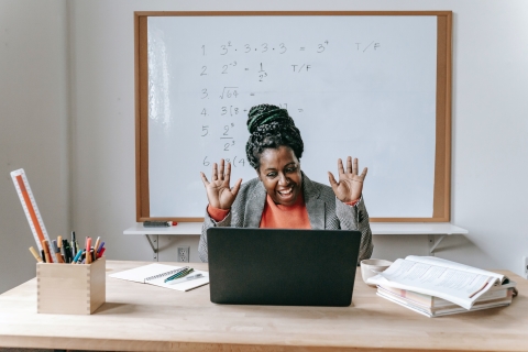 Teacher in classroom waving to her laptop screen