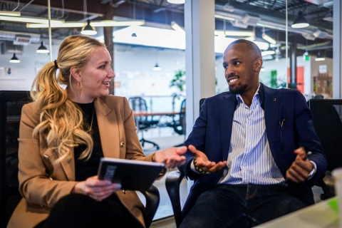 Two people sitting, talking and holding a tablet in an office