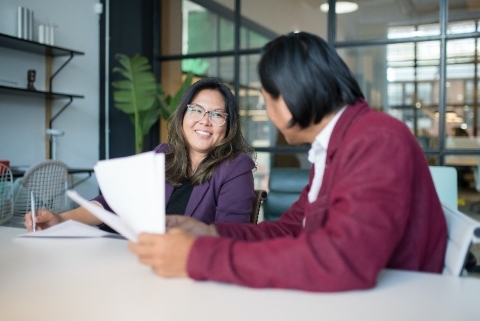 Two people smiling at each other while sitting at a conference table