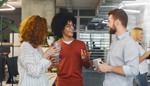 3 people standing in an office with coffee cups talking